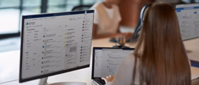Two professionals working on computers with large screens displaying a project management software interface