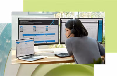 Woman with headphones working on multiple computer screens and a laptop in a modern office setting.