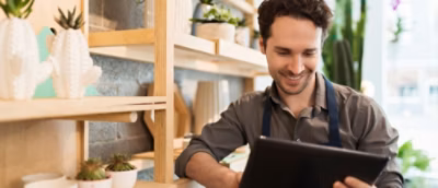 A man wearing an apron and looking at a tablet.