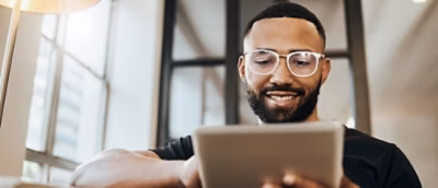 A man wearing glasses and looking at a tablet.