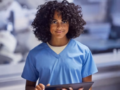 A person wearing a blue scrub, holding a tablet and smiling.
